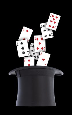 Vertical shot of playing cards spilling out from a black top hat isolated on a black background A vertical shot of playing cards spilling out from a black top hat isolated on a black background, magician concept